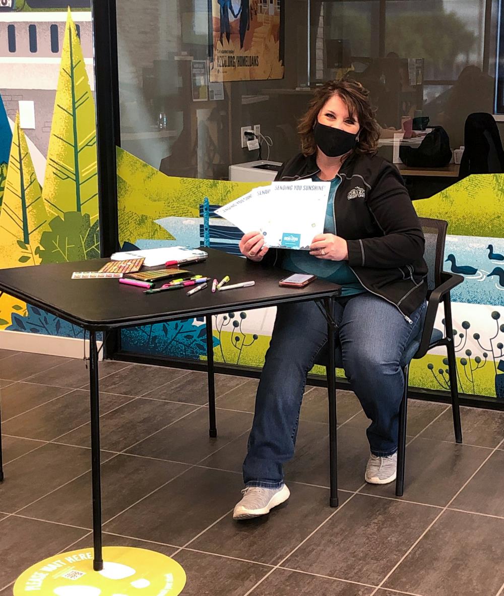 Employee sitting at table holding up written cards, wearing a mask