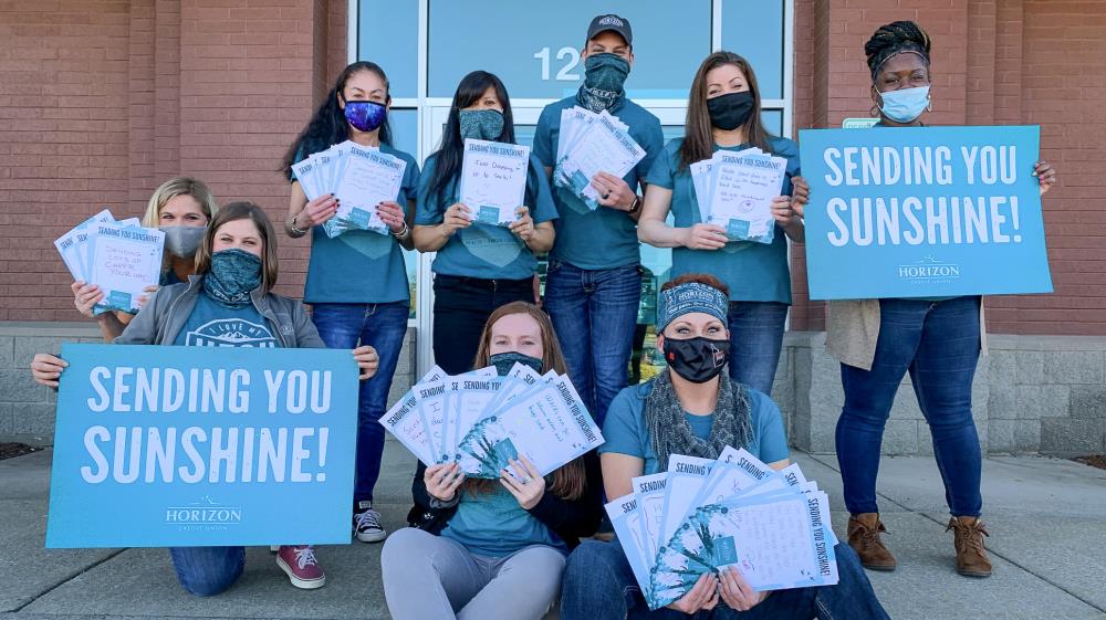 Team of employees wearing masks holding up cards they made and signs that say 