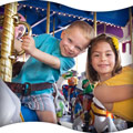 Image of two smiling young kids on a carousel ride