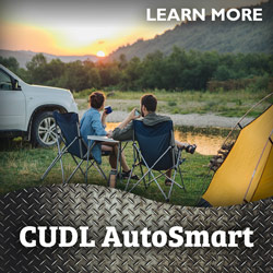 Image of a couple relaxing in lawn chairs at their camping site by a river with their vehicle parked nearby