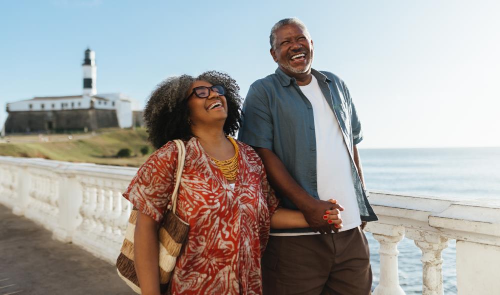 Retired Couple Touring a Beach with a LIghthouse in the Background
