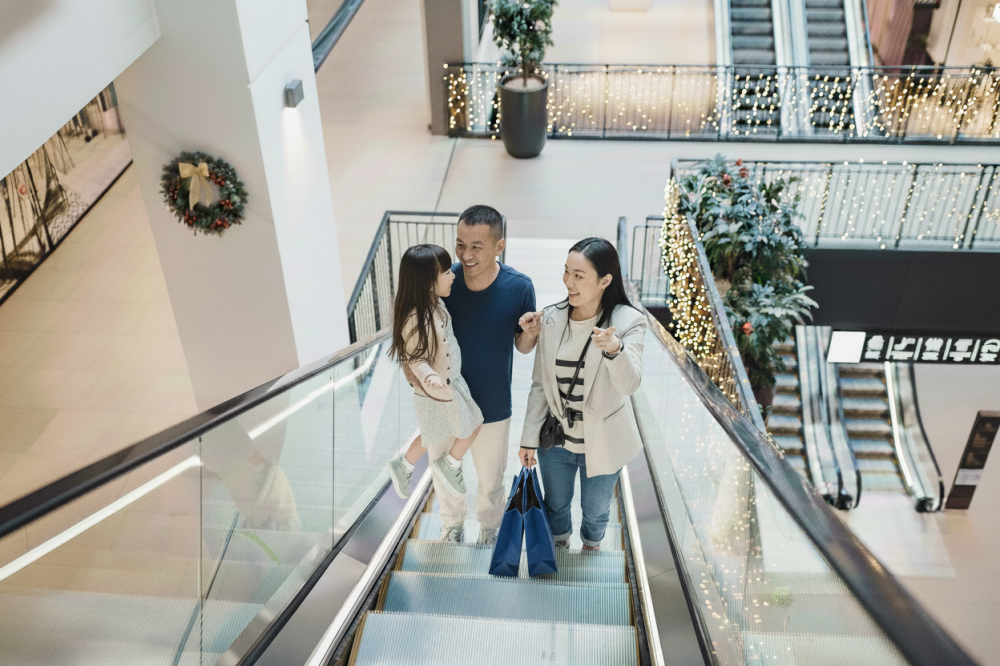Family riding escalator in mall, pointing out the holiday decorations while shopping.