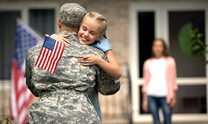 Man in military uniform hugging child with American flag